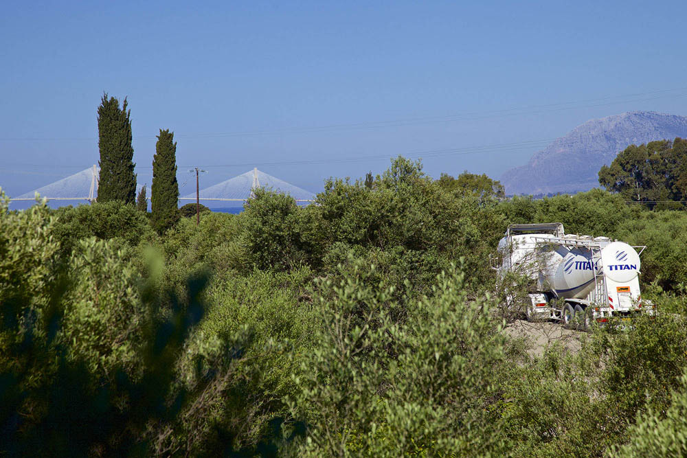 TITAN track on a road filled trees and Rion-Antirion Bridge, at the background